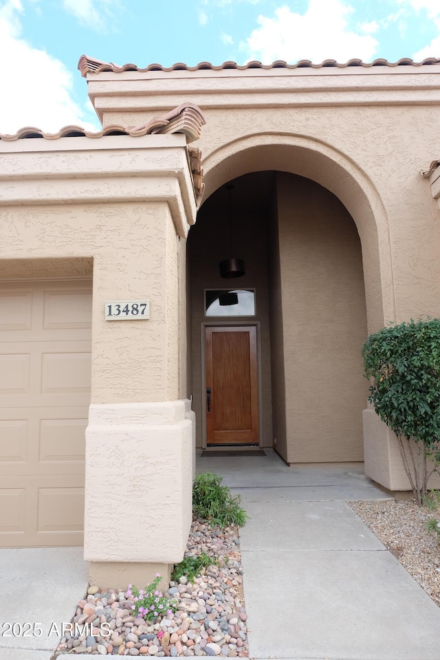 view of exterior entry with a garage and stucco siding