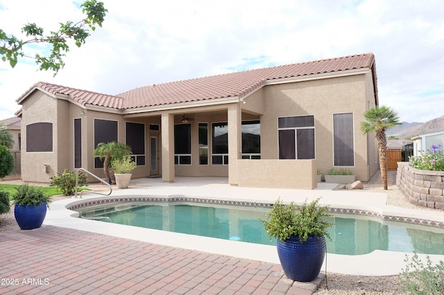 back of property with fence, an outdoor pool, stucco siding, a tile roof, and a patio area