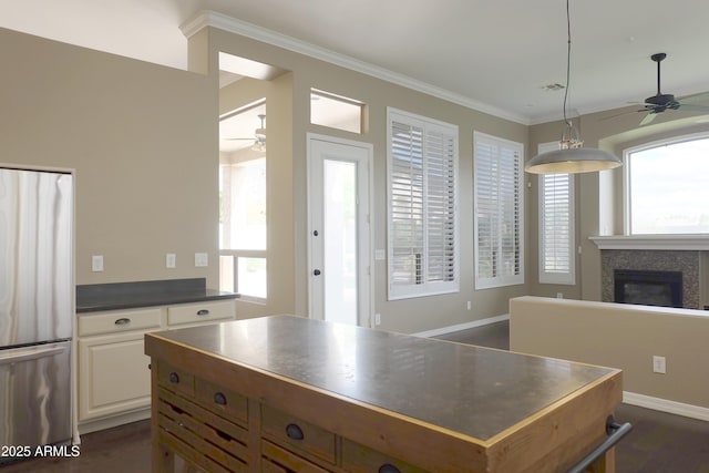 kitchen with dark countertops, a glass covered fireplace, freestanding refrigerator, crown molding, and ceiling fan