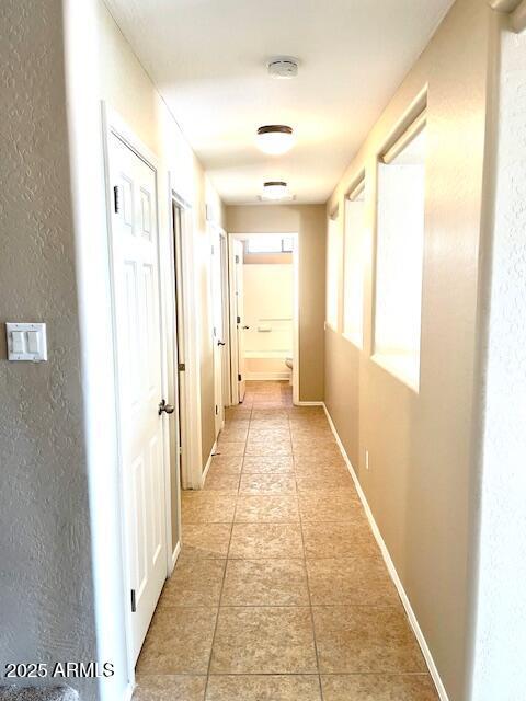 hallway featuring a textured wall, baseboards, and light tile patterned floors