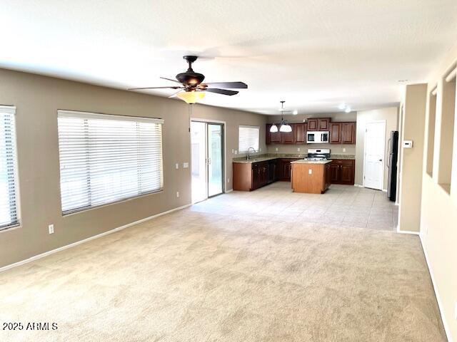 kitchen with light carpet, a kitchen island, light countertops, hanging light fixtures, and stainless steel microwave