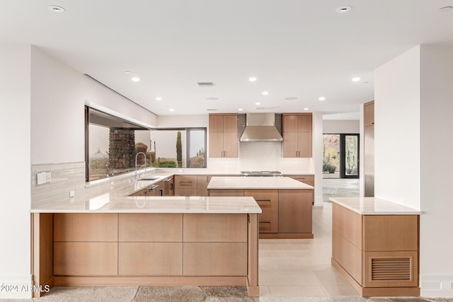 kitchen featuring visible vents, modern cabinets, a peninsula, wall chimney range hood, and backsplash