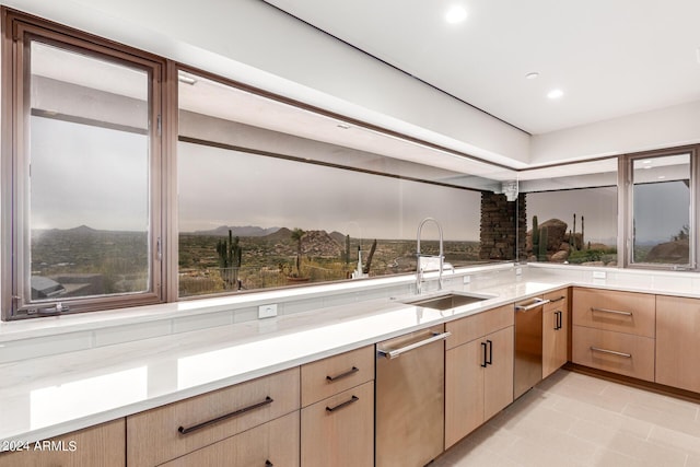 kitchen featuring a mountain view, sink, stainless steel dishwasher, light tile patterned floors, and light brown cabinetry