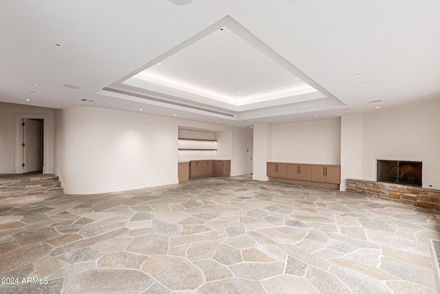 unfurnished living room featuring a fireplace with raised hearth, a tray ceiling, baseboards, and stone flooring