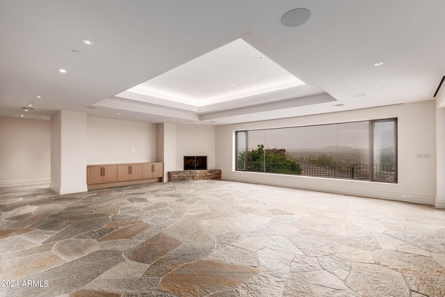 unfurnished living room with baseboards, stone flooring, a tray ceiling, and recessed lighting