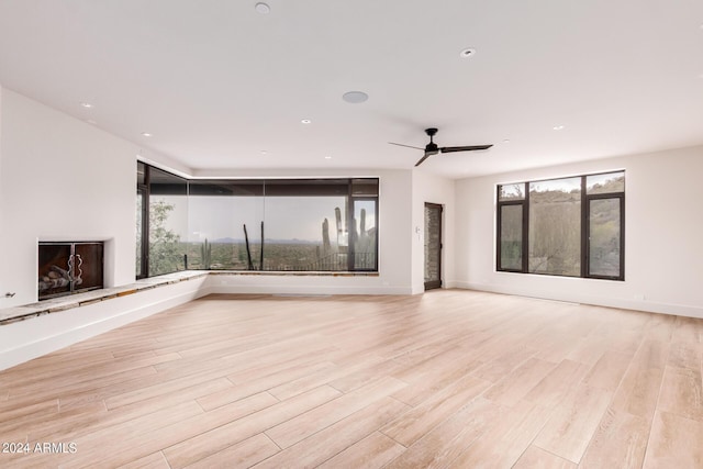 unfurnished living room with a fireplace with raised hearth, light wood finished floors, recessed lighting, and baseboards