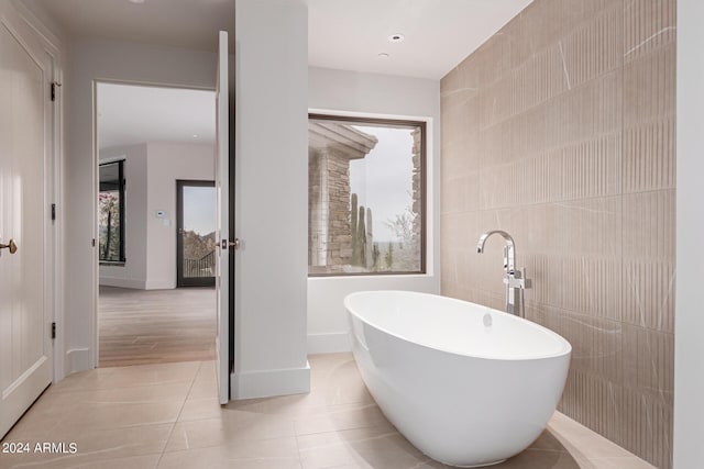 bathroom with tile patterned flooring, a freestanding tub, and tile walls