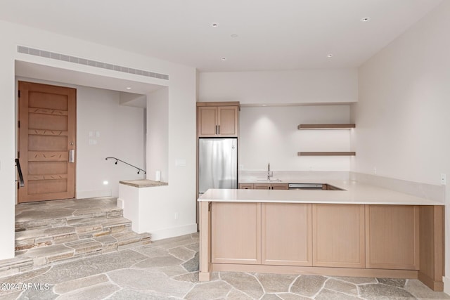 kitchen featuring kitchen peninsula, stainless steel refrigerator, light brown cabinetry, and sink