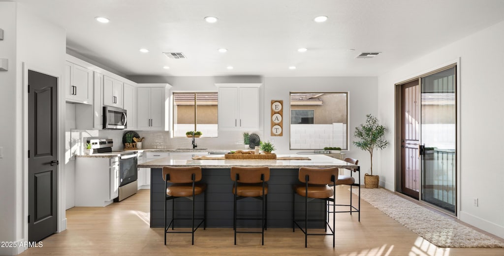 kitchen featuring stainless steel appliances, light hardwood / wood-style flooring, white cabinets, a kitchen island, and a breakfast bar area