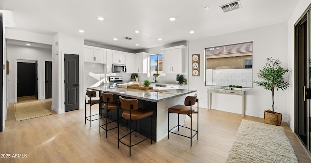 kitchen featuring light stone countertops, stove, white cabinets, a center island, and a breakfast bar area