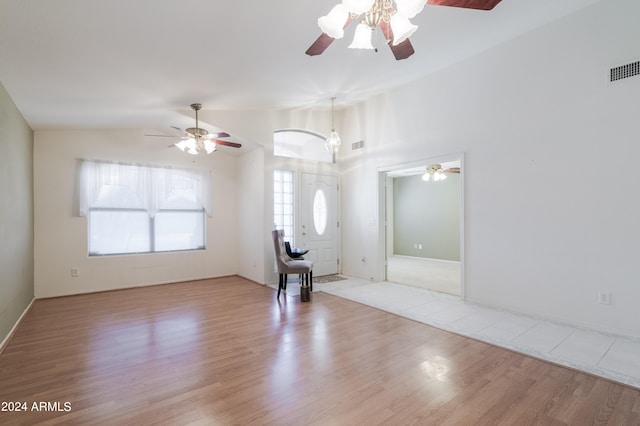 unfurnished living room with vaulted ceiling, ceiling fan with notable chandelier, and light hardwood / wood-style floors