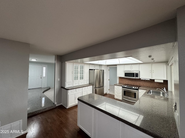 kitchen with a sink, dark wood-type flooring, white cabinets, appliances with stainless steel finishes, and dark countertops