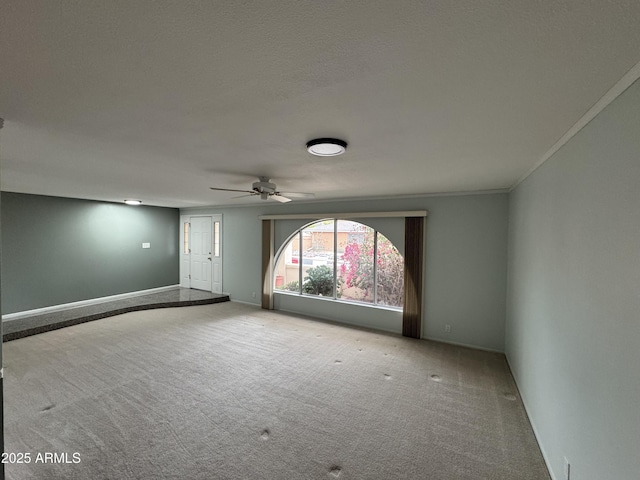 spare room featuring crown molding, carpet flooring, a ceiling fan, and baseboards