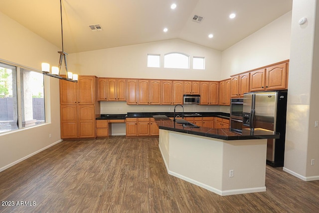 kitchen featuring appliances with stainless steel finishes, dark hardwood / wood-style flooring, a center island with sink, high vaulted ceiling, and hanging light fixtures