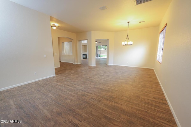 unfurnished living room with ceiling fan with notable chandelier and dark wood-type flooring