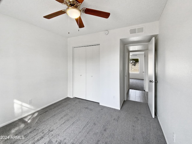 unfurnished bedroom with ceiling fan, a closet, a textured ceiling, and dark colored carpet