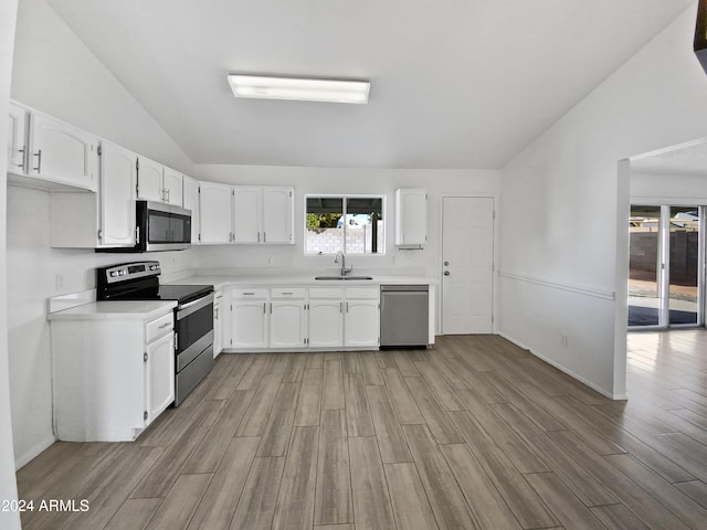 kitchen with light wood-type flooring, stainless steel appliances, sink, white cabinetry, and lofted ceiling