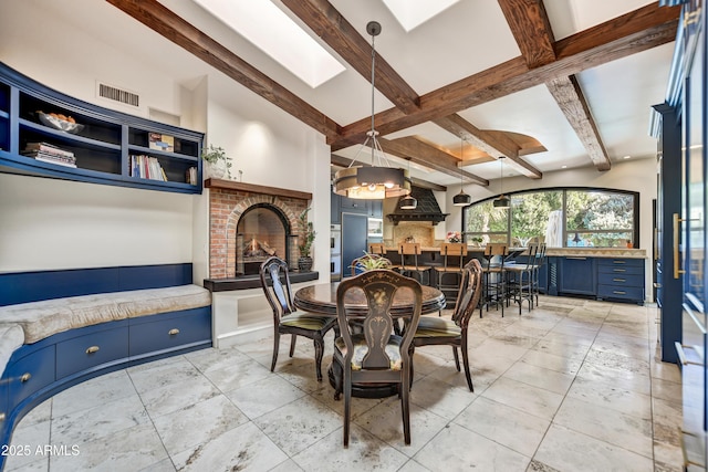 dining area featuring a brick fireplace, a skylight, and beamed ceiling