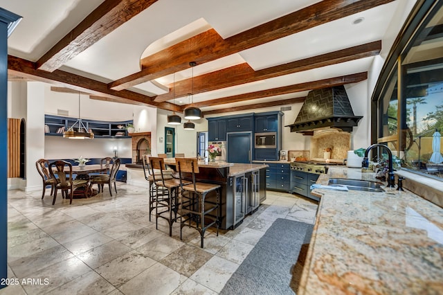 kitchen with sink, a kitchen breakfast bar, hanging light fixtures, custom range hood, and blue cabinets