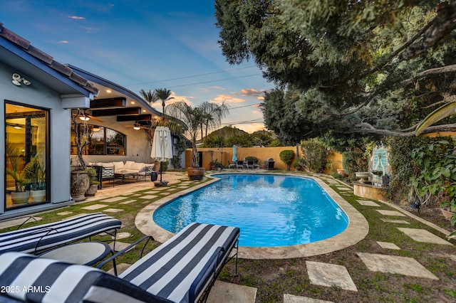 pool at dusk with ceiling fan, a patio area, and outdoor lounge area