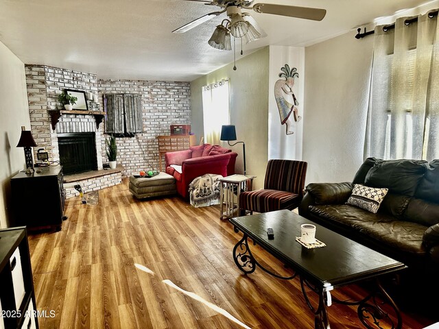 living area featuring ceiling fan, a textured ceiling, a brick fireplace, and light wood-style floors