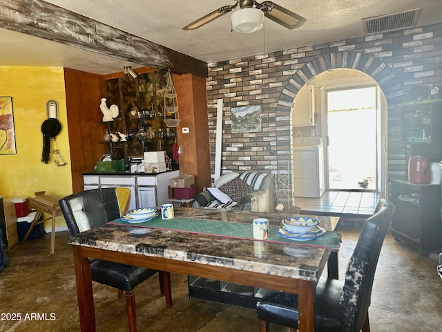 dining area with ceiling fan, a textured ceiling, arched walkways, visible vents, and washer / dryer