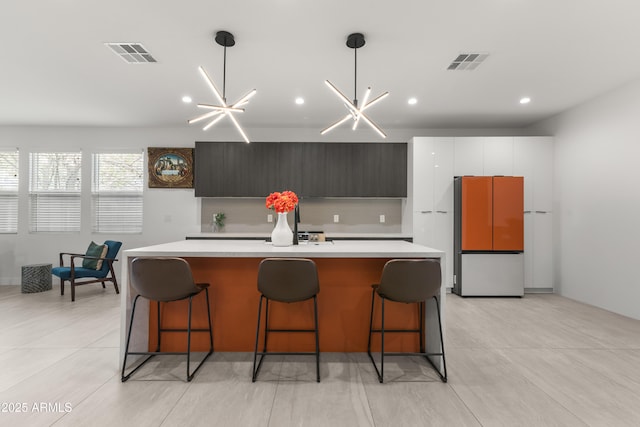 kitchen featuring pendant lighting, tasteful backsplash, a kitchen bar, fridge, and a kitchen island with sink