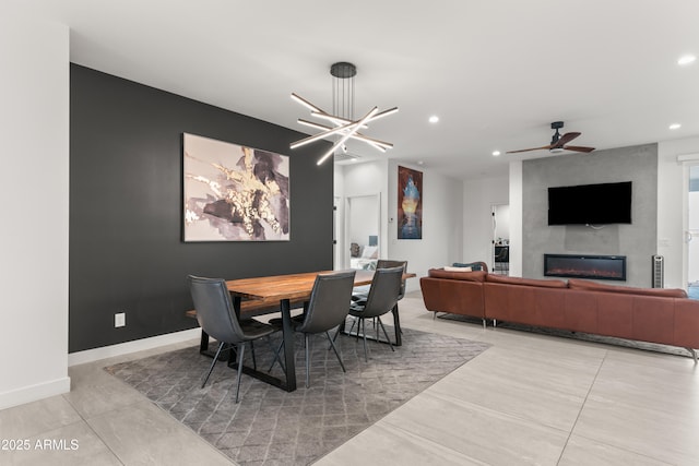 dining area featuring a large fireplace and ceiling fan with notable chandelier