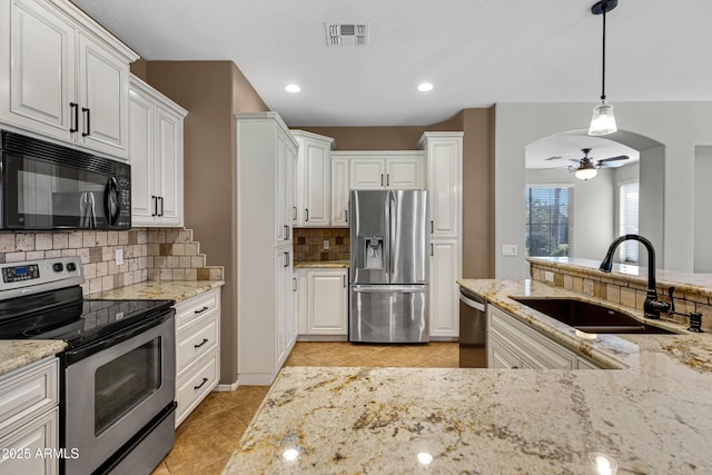 kitchen with sink, light stone counters, appliances with stainless steel finishes, pendant lighting, and white cabinets