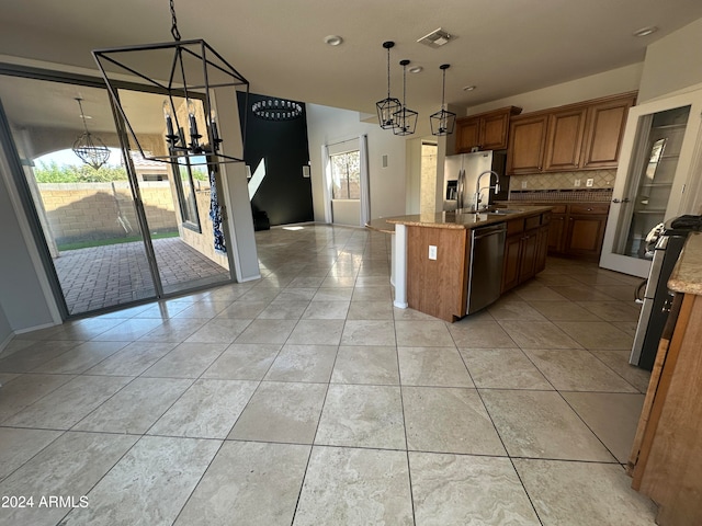 kitchen with light stone countertops, tasteful backsplash, hanging light fixtures, appliances with stainless steel finishes, and a center island with sink