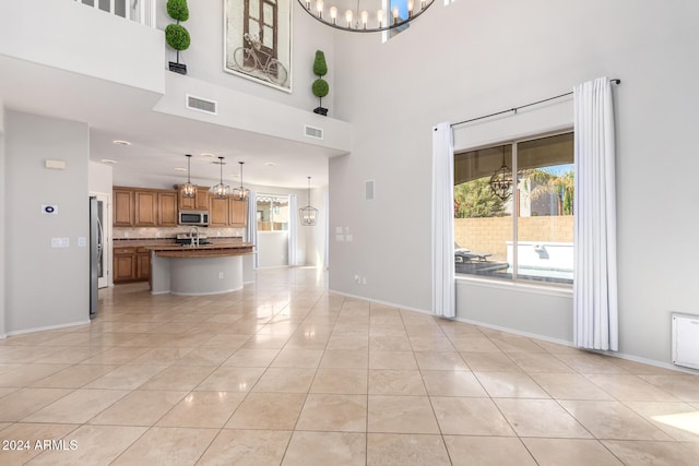 unfurnished living room with a notable chandelier, sink, a towering ceiling, and light tile patterned floors