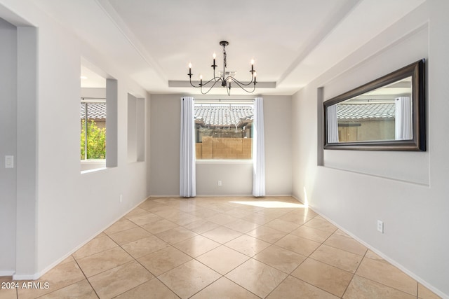 tiled spare room featuring a notable chandelier and a tray ceiling