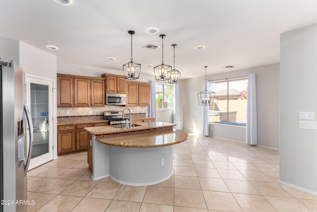 kitchen with pendant lighting, sink, a kitchen island with sink, appliances with stainless steel finishes, and light stone countertops