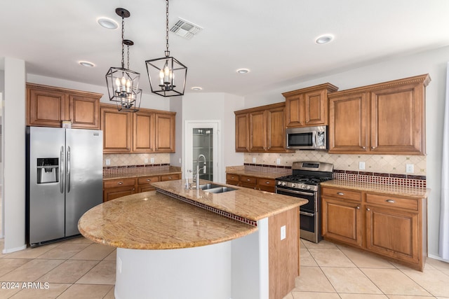 kitchen with an island with sink, hanging light fixtures, appliances with stainless steel finishes, light tile patterned floors, and backsplash