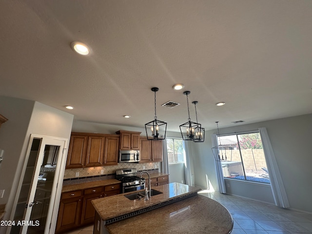 kitchen with backsplash, a notable chandelier, sink, stainless steel appliances, and an island with sink