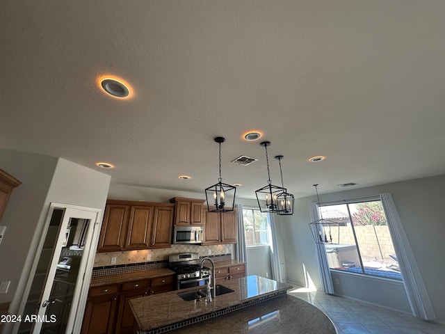 kitchen with an island with sink, light tile patterned floors, stainless steel appliances, an inviting chandelier, and decorative backsplash