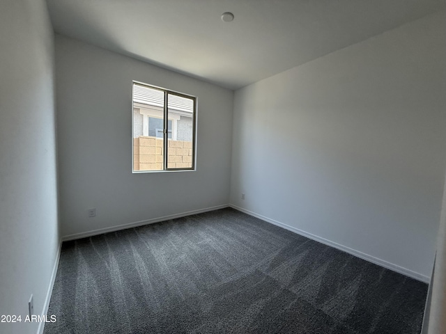 unfurnished room with baseboards and dark carpet