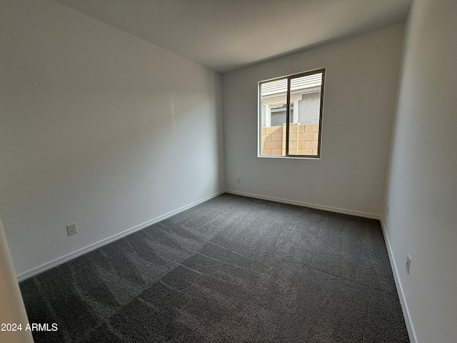 spare room with baseboards and dark colored carpet