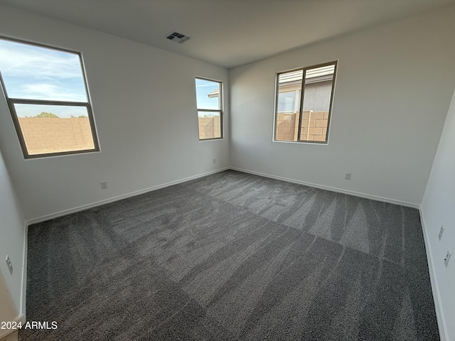 empty room with baseboards, dark carpet, and visible vents