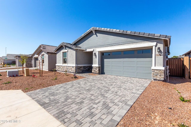 view of front of house with stone siding, fence, a garage, stucco siding, and driveway