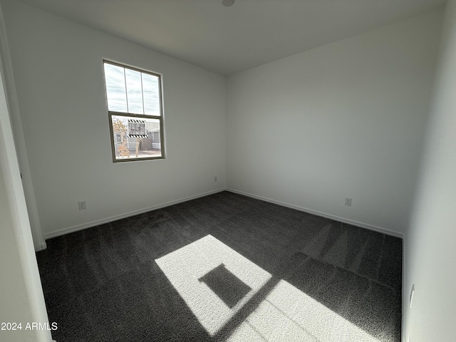 spare room with baseboards and dark colored carpet