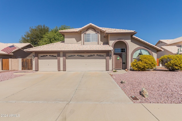 mediterranean / spanish home with a tile roof, stucco siding, concrete driveway, and fence