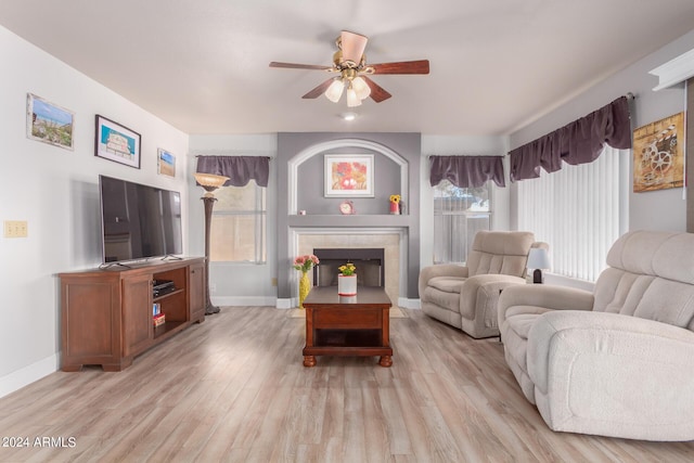 living area featuring baseboards, a ceiling fan, a tiled fireplace, and light wood finished floors