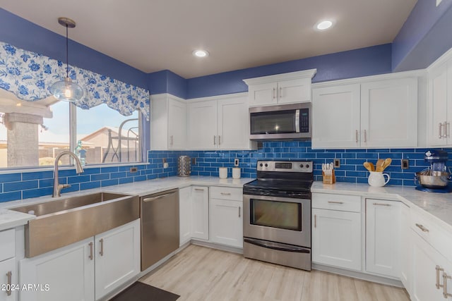 kitchen featuring light wood-type flooring, a sink, backsplash, stainless steel appliances, and white cabinets