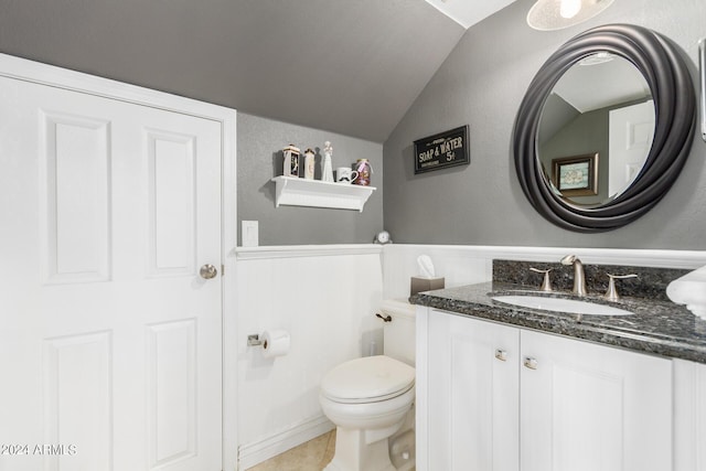 half bathroom with vanity, a wainscoted wall, lofted ceiling, tile patterned flooring, and toilet