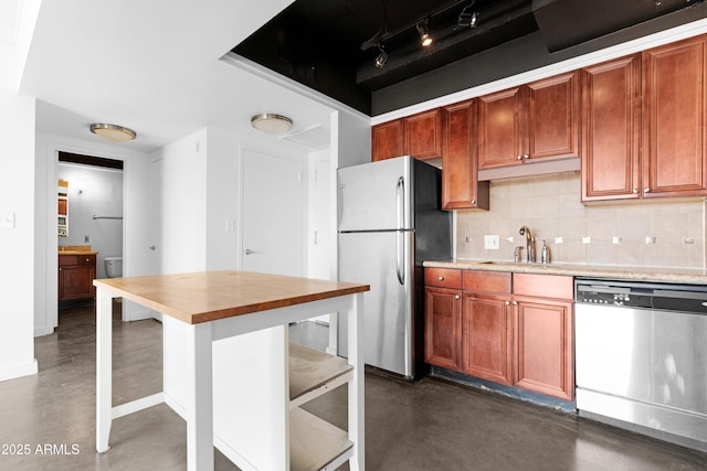 kitchen with finished concrete flooring, track lighting, appliances with stainless steel finishes, a sink, and decorative backsplash