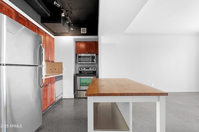 kitchen featuring finished concrete flooring, rail lighting, appliances with stainless steel finishes, wood counters, and backsplash