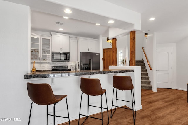 kitchen with wood-type flooring, white cabinetry, backsplash, kitchen peninsula, and appliances with stainless steel finishes