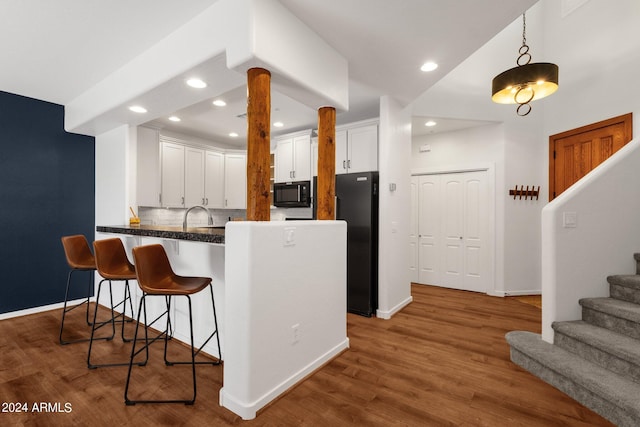 kitchen featuring kitchen peninsula, backsplash, black appliances, hardwood / wood-style flooring, and white cabinetry