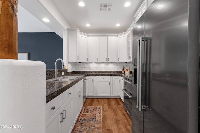 kitchen with appliances with stainless steel finishes, white cabinets, sink, tasteful backsplash, and wood-type flooring